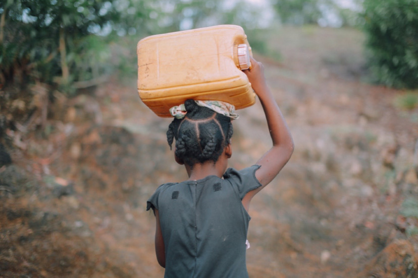 A girl carrying a jerrycan on a head.