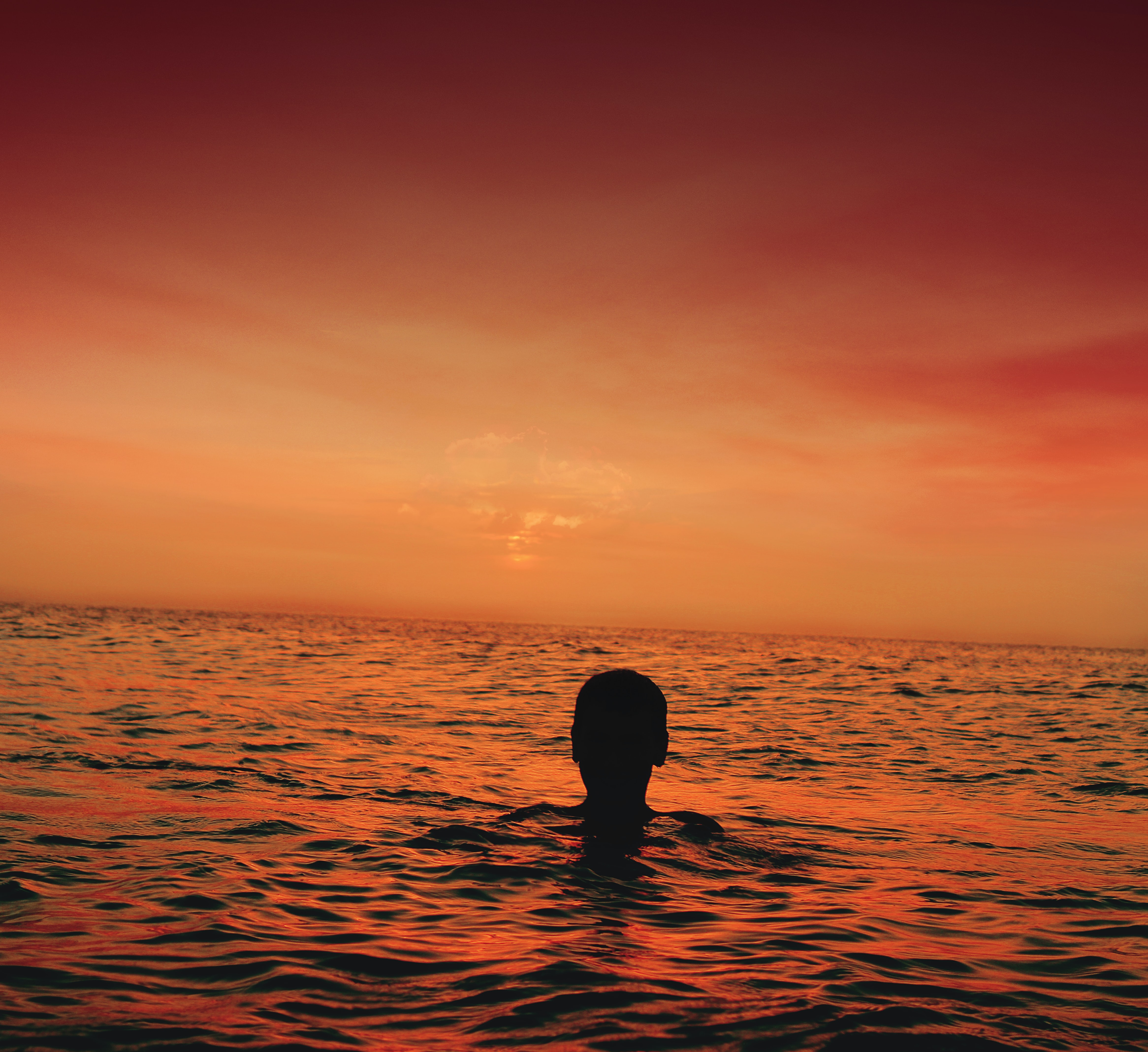 Silhouette of person in ocean during sunset.